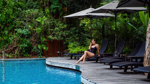 Tan young model in black bikini, posing and relaxing by swimming pool © TravelMedia