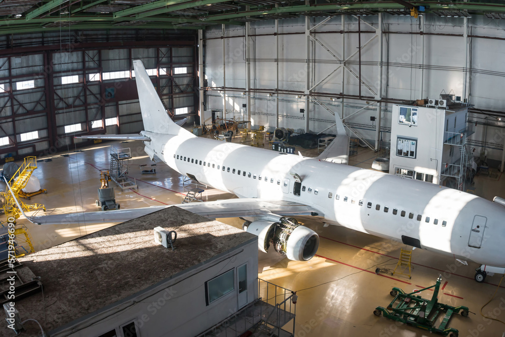 Top view of a white passenger aircraft in the hangar. Airplane under maintenance. Checking mechanical systems for flight operations Top view of a white passenger aircraft in the hangar. Airplane under maintenance. Checking mechanical systems for flight operations