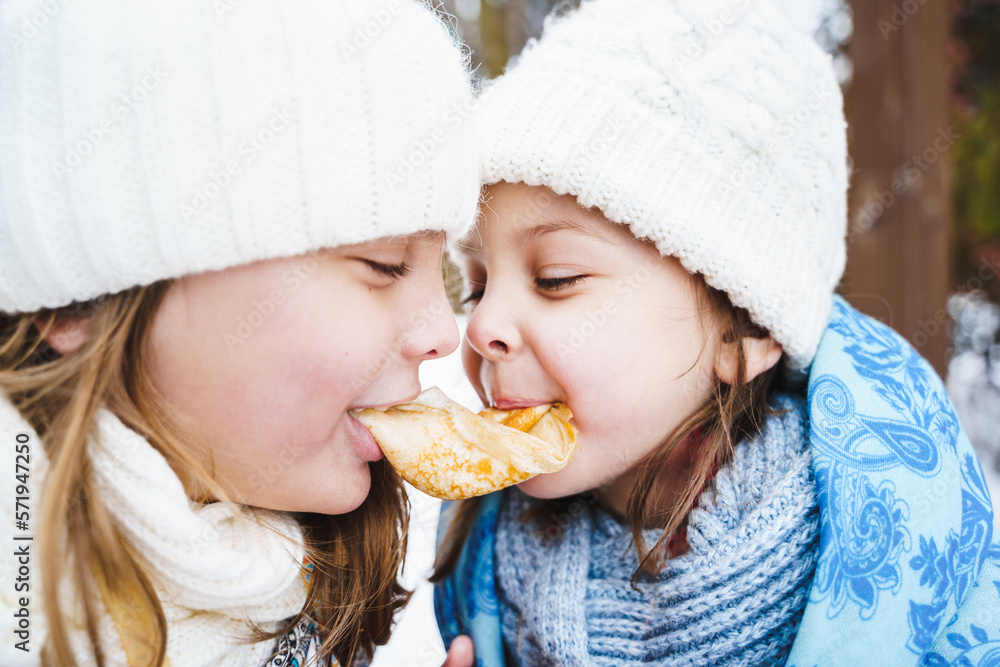 Russian national festival Maslenitsa, shrovetide. Little cute beautiful girls in headscarf eat big tasty pancakes, have fun on winter pancake holiday week. Traditional folf slavic street carnival Russian national festival Maslenitsa, shrovetide. Little cute beautiful girls in headscarf eat big tasty pancakes, have fun on winter pancake holiday week. Traditional folf slavic street carnival