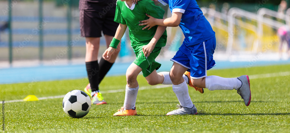 Kids Football Players Kicking Ball on Soccer Field. Sports Soccer Horizontal Background. Stadium in the Background. Youth Junior Athletes in Green and Blue Soccer Shirts. Sports Education Kids Football Players Kicking Ball on Soccer Field. Sports Soccer Horizontal Background. Stadium in the Background. Youth Junior Athletes in Green and Blue Soccer Shirts. Sports Education