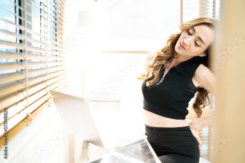 beautiful woman stretching back tired working using laptop. pretty female worker hurt from office syndrome over work late bending back prevent pain. gorgeous freelancer heal back after do task late