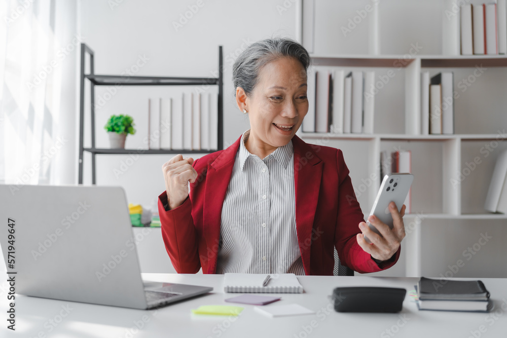 Asian elderly older female mature business woman in formal suit stock trader on stock market and money exchange rate trading working in modern office workplace. Asian elderly older female mature business woman in formal suit stock trader on stock market and money exchange rate trading working in modern office workplace.