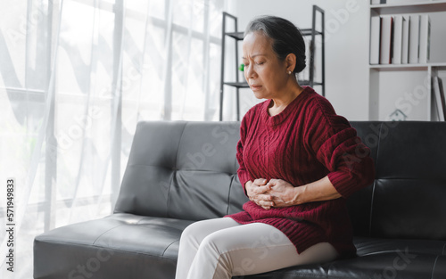 Elderly asian housewife woman sitting on sofa. Abdominal pain, gastritis, appendicitis