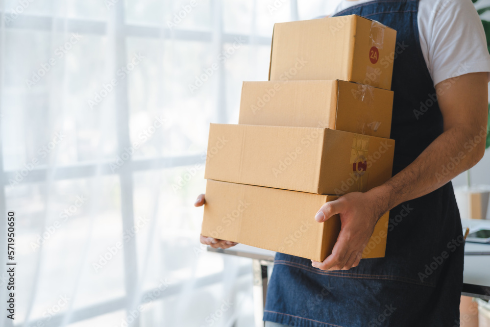 Young asian sme business man in apron working at warehouse home office freelancer retail logistic company with package box checking customer address. Young asian sme business man in apron working at warehouse home office freelancer retail logistic company with package box checking customer address.