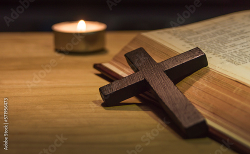 cross and bible with a lit candle on the background