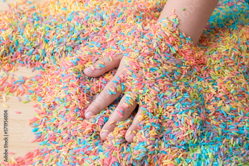Two hands mixing colourful sensory bin