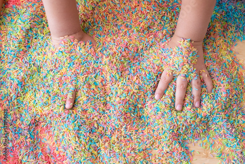 Two hands mixing colourful sensory bin