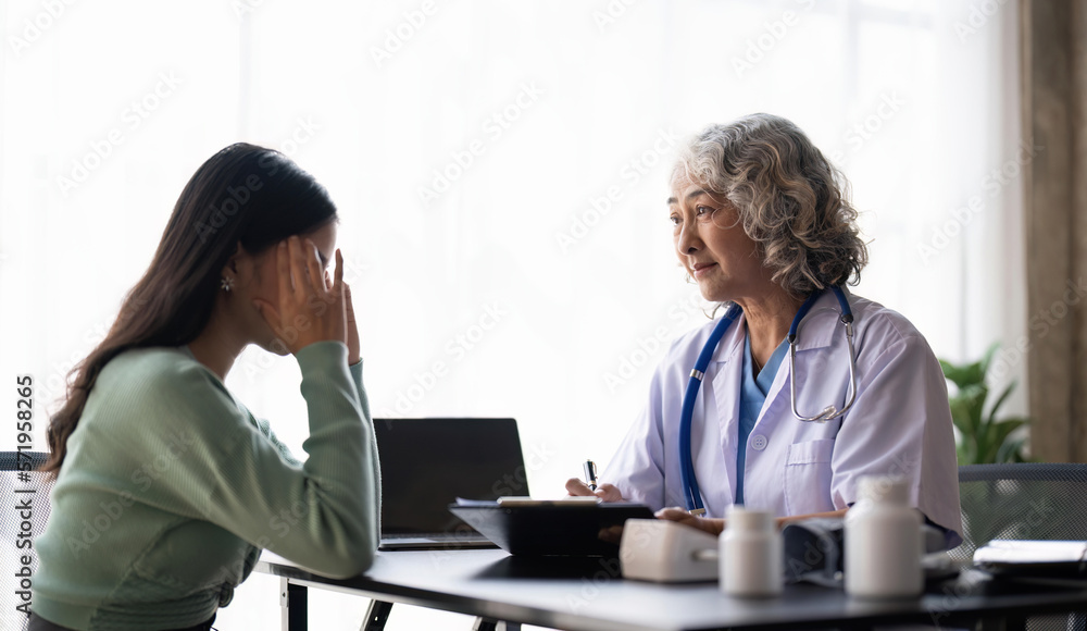 Woman senior doctor is Reading Medical History of Female Patient and Speaking with Her During Consultation in a Health Clinic. Physician in Lab Coat Sitting Behind a Laptop in Hospital Office Woman senior doctor is Reading Medical History of Female Patient and Speaking with Her During Consultation in a Health Clinic. Physician in Lab Coat Sitting Behind a Laptop in Hospital Office