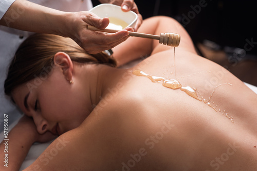 young woman lying on the table and getting spa procedure massage with honeyed in dark room