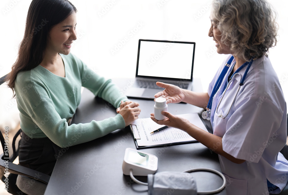 Woman senior doctor is Reading Medical History of Female Patient and Speaking with Her During Consultation in a Health Clinic. Physician in Lab Coat Sitting Behind a Laptop in Hospital Office Woman senior doctor is Reading Medical History of Female Patient and Speaking with Her During Consultation in a Health Clinic. Physician in Lab Coat Sitting Behind a Laptop in Hospital Office