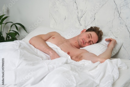 Young handsome naked man is sleeping in bed in bedroom on pillow