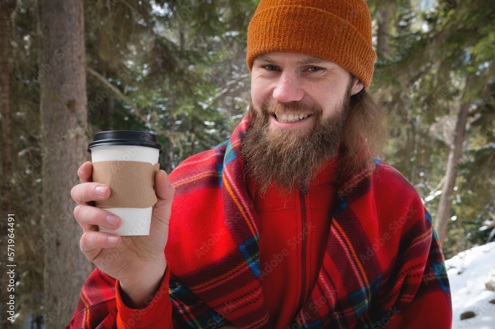 Walk with a cup of hot cocoa in the winter park. Portrait of a handsome bearded guy in winter clothes in the snow drinking hot tea or coffee from a paper cup and enjoying a nice sunny snowy day Walk with a cup of hot cocoa in the winter park. Portrait of a handsome bearded guy in winter clothes in the snow drinking hot tea or coffee from a paper cup and enjoying a nice sunny snowy day