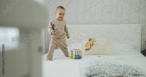 Baby child playing with toys on the bed in bedroom, toddler kid having fun at home