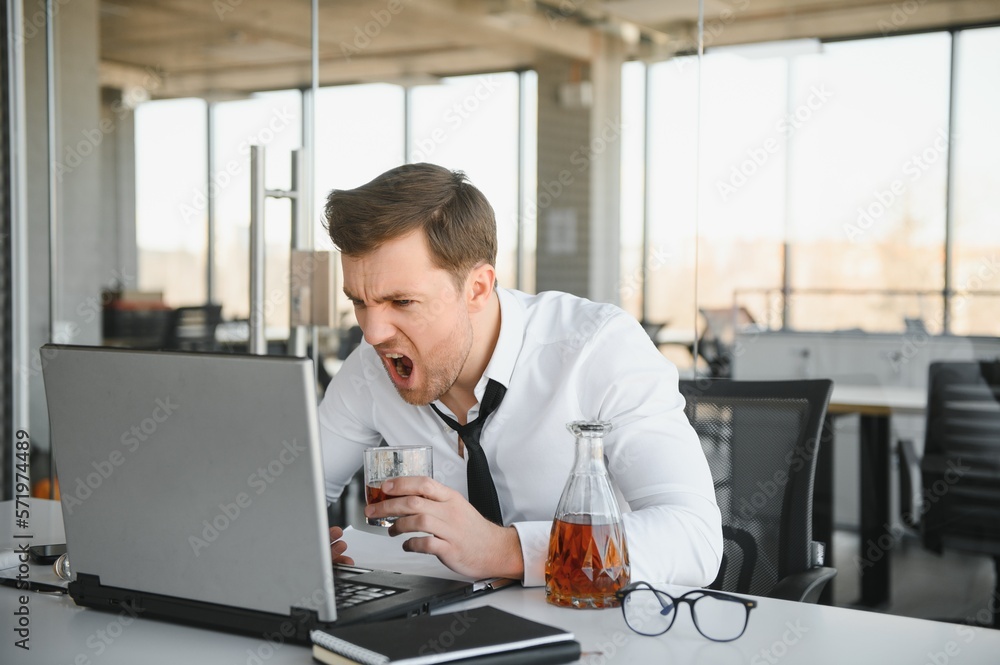 Young stressed handsome businessman working at desk in modern office shouting at laptop screen and being angry about financial situation, jealous of rival capabilities, unable to meet client needs Young stressed handsome businessman working at desk in modern office shouting at laptop screen and being angry about financial situation, jealous of rival capabilities, unable to meet client needs