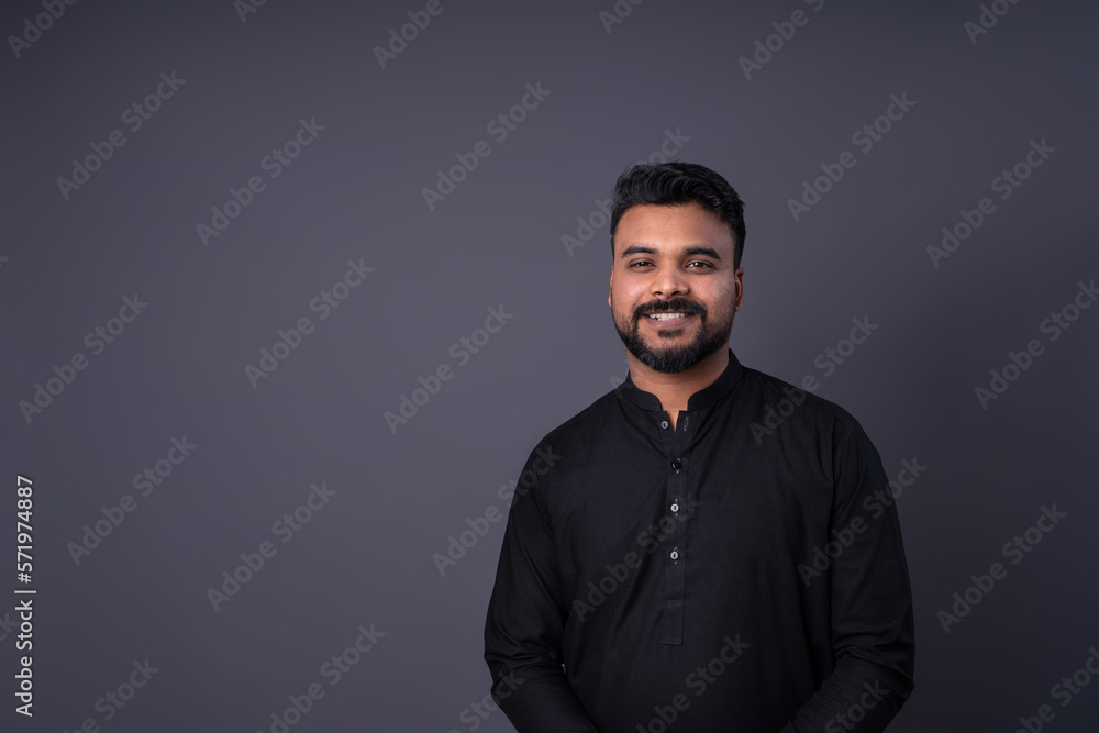 Obraz premium Smiling an with dark hair with mustache and beard portrait on gray background. Horizontal banner empty template gray copy space. Pakistani young man in traditional black shirt clothes