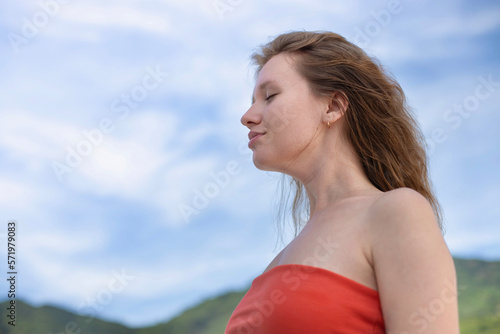Portrait of happy beautiful young girl, dreams and meditation, relax nature, tanning on sun at summer sunny day on natural background with sky and mountains, breathing deep fresh air 