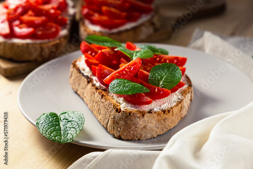 Front view of three pieces of bruschetta on a plate with cherry tomatoes  cream cheese and mint leaves on a wooden table