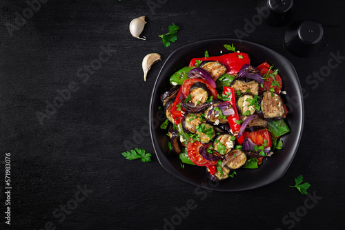 Grilled vegetables eggplant, bell pepper, zucchini, red onion, tomato with garlic on a black plate. Top view, above