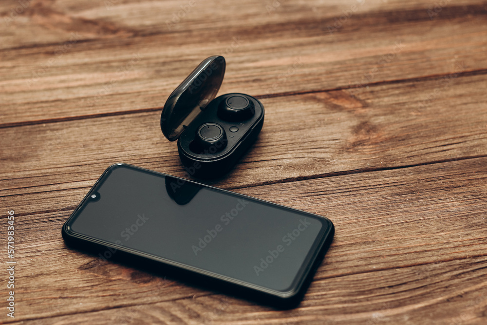 Wireless headphones in a black box on the table next to the phone. Wireless headphones in a black box on the table next to the phone.