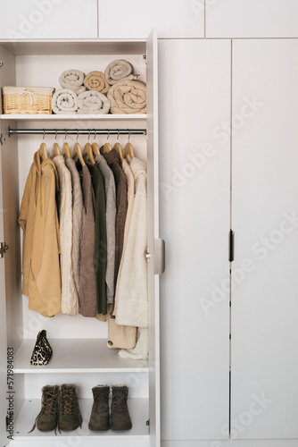 The basic wardrobe of a fashion stylist. Neutral colors: white, brown, beige, grey. White wardrobe, wooden hangers, towels, shoes and bag