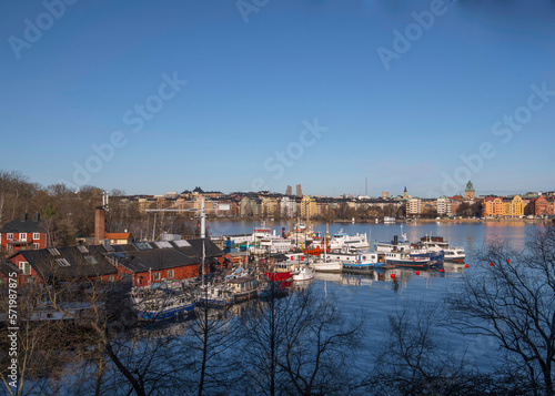 View from the district Södermalm over the bay Riddarfjärden with the Town City Hall and down town, wharf with fishing, tug and steam commuting boats, a sunny winter day in Stockholm