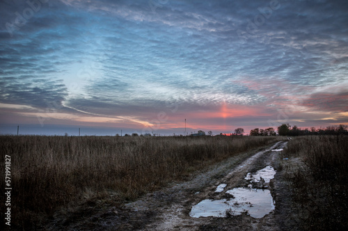The field road between the villages is covered with puddles that reflect the colors of the dawn sun. © Галина Нечипорук