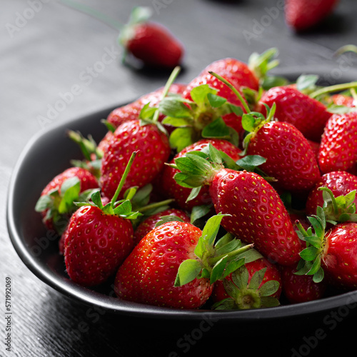 Strawberries in a black plate on dark background.