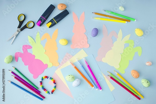 Easter spring holiday. Craft, children's creativity, cute multi-colored rabbits cut out of paper lie on a blue background. Flat lay, top view pattern.