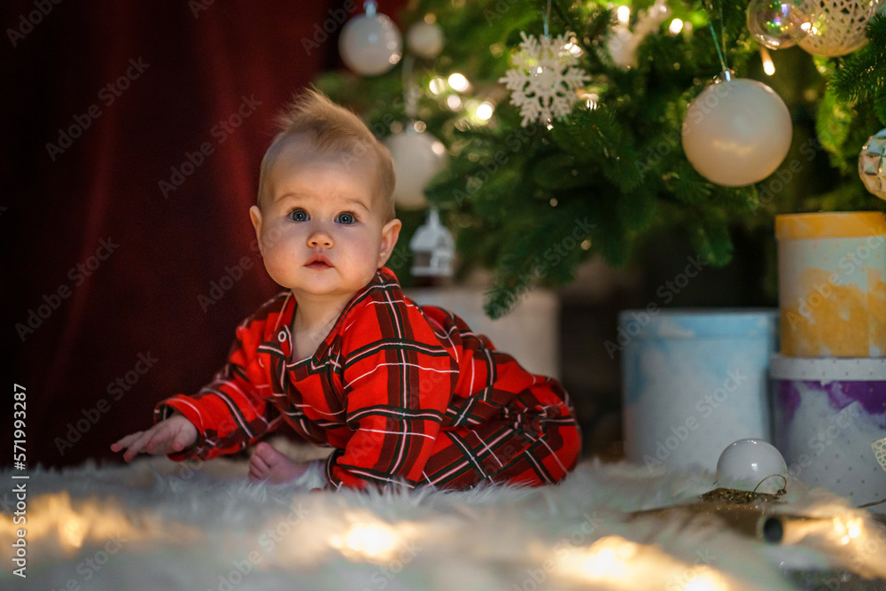 Cute little baby toddler near the Christmas tree playing with a garland and toys. The concept of the new year and Christmas mood Cute little baby toddler near the Christmas tree playing with a garland and toys. The concept of the new year and Christmas mood