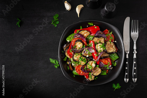 Grilled vegetables eggplant, bell pepper, zucchini, red onion, tomato with garlic on a black plate. Top view, above
