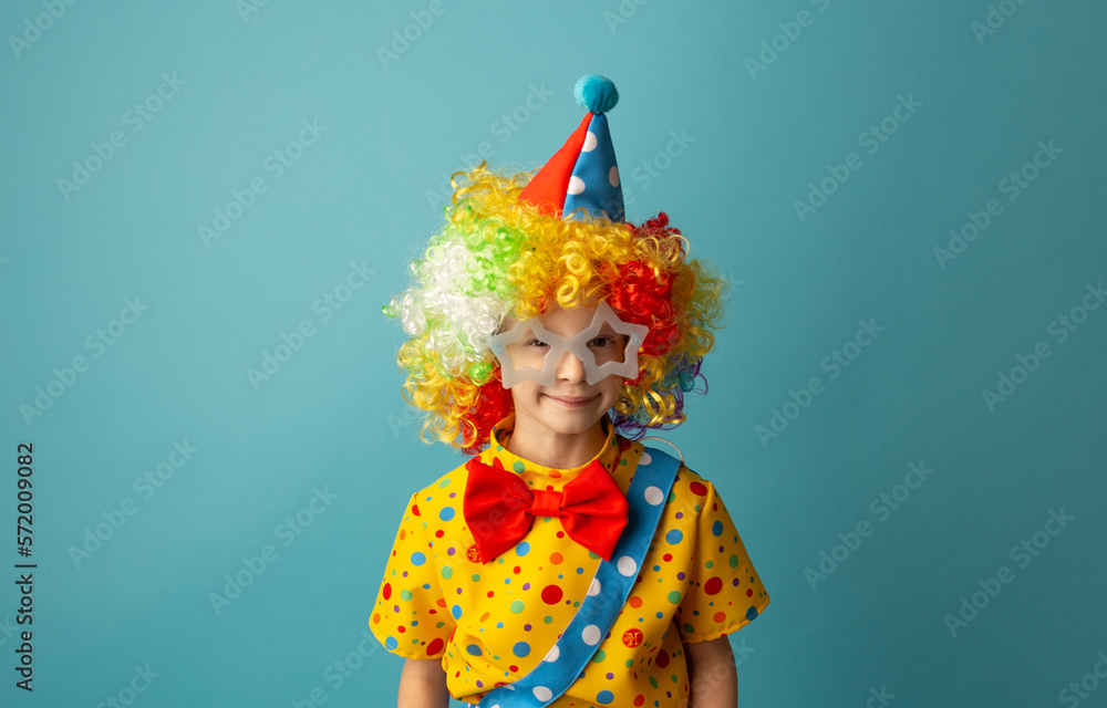 Funny kid clown against blue background. Happy child playing with festive decor. 1 April Fool's day concept Funny kid clown against blue background. Happy child playing with festive decor. 1 April Fool's day concept
