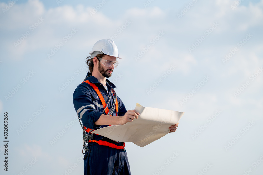 Smart engineer or technician man stand with holding drawiing paper and look to paper with background of blue sky. Smart engineer or technician man stand with holding drawiing paper and look to paper with background of blue sky.