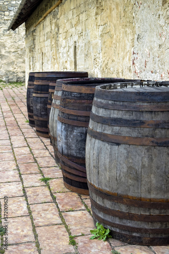 Old large oak barrels with rusty hoops are arranged in row along ancient stone wall. Copy space. Selective focus.