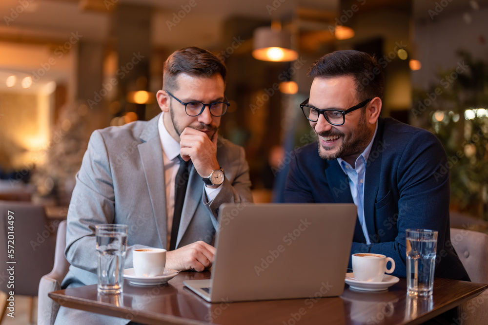 Two businessmen, elegant stylish corporate leaders, successful CEO executive managers on meeting in Cafe or restaurant working on laptop, discussing and analyzing business plan, developing strategy.