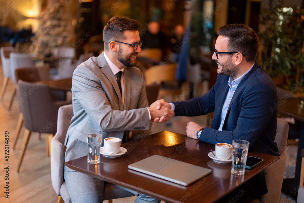 Two smiling confident male business partners at business meeting in restaurant shaking hands as sign they have reached an agreement, finishing up a meeting or setting goals, sharing productive ideas.