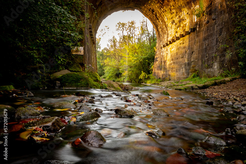 Stream with an autumn leaves and pebbles under a viaduct in Daisy Nook park Oldham England