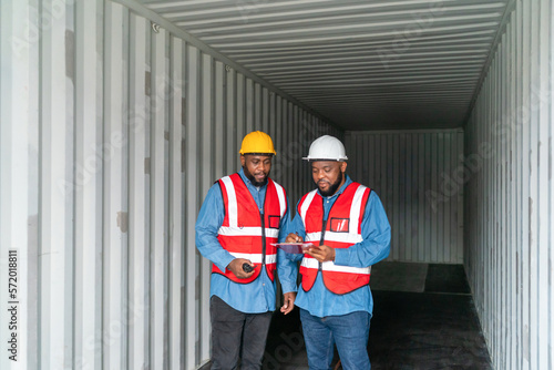 Portrait of Two African Engineer or foreman wears PPE checking container storage with cargo container background at sunset. Logistics global import or export shipping industrial concept.