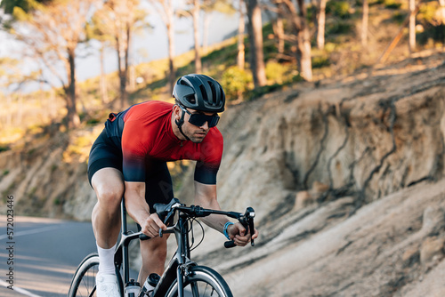 Professional cyclist going down a hill. Athlete in helmet and glasses riding road bike outdoors.