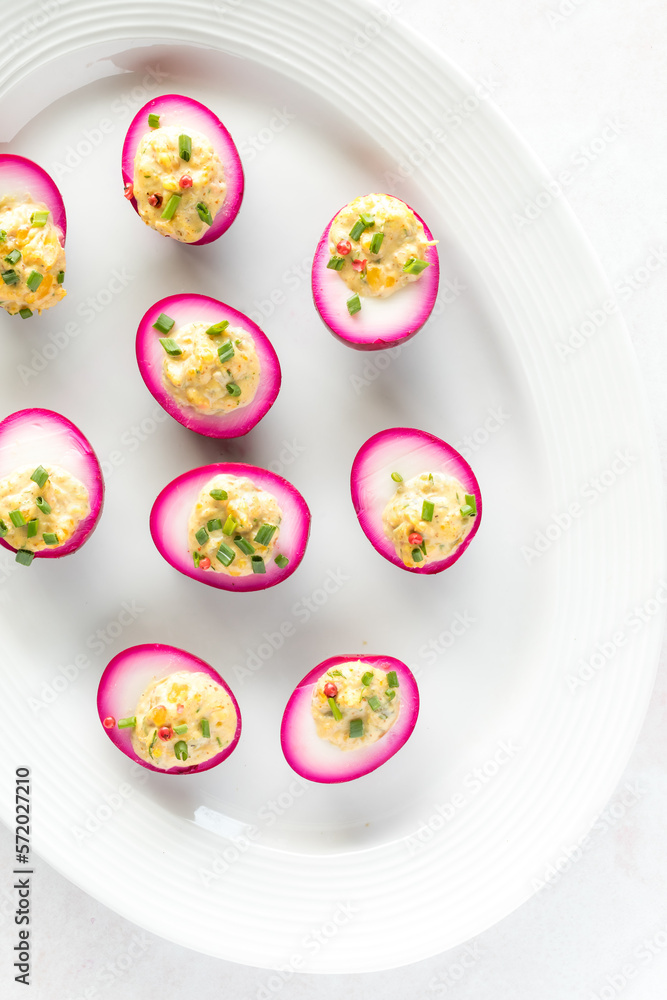Top down view of a platter of beet juice dyed Deviled eggs, ready for eating.