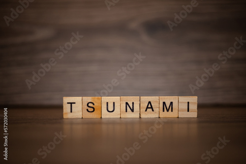 The word tsunami is made up of wooden cubes tablets on a dark wooden background