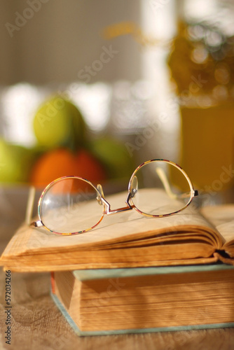 Cup of tea, plates with cookies, glass of orange juice, books, reading glasses, bowl of fruit and candles on the table. Selective focus.