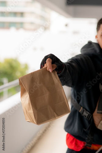 hand of young app latino fast food delivery man delivering package in paper bag. Dominican man