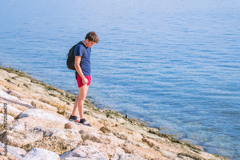 A teenager boy men looking for stone crabs at stones near the water, sunny day near sea