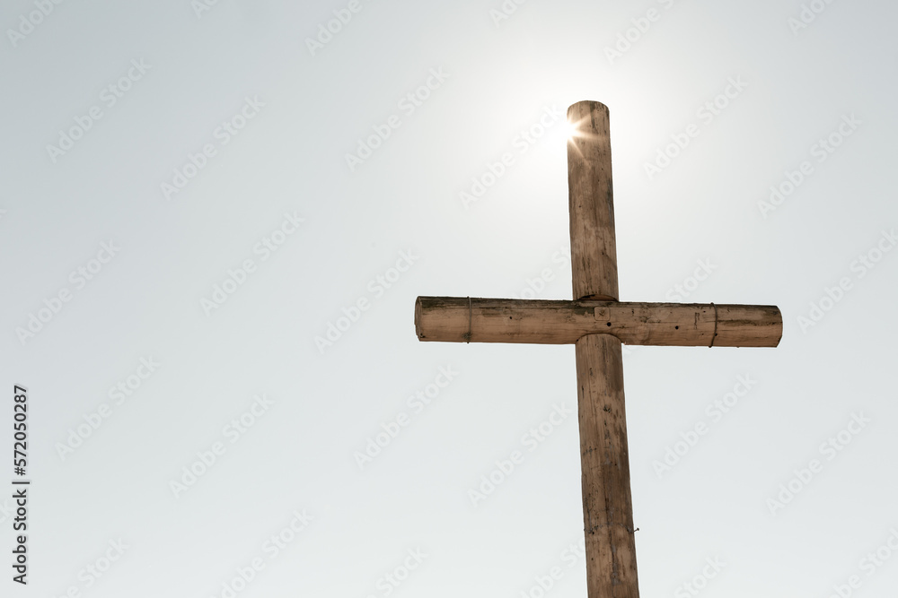 Sun shining on brown rustic wooden cross against sky Sun shining on brown rustic wooden cross against sky