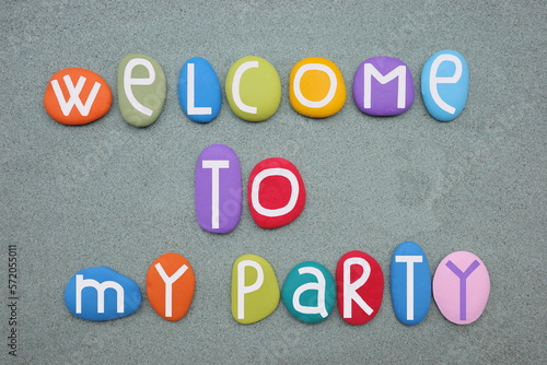 Welcome to my party, creative message composed with multi colored stone letters over green sand