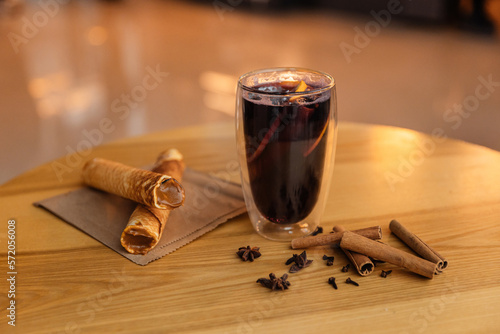 A transparent glass with mulled wine on a table in a coffee shop. Hot mulled wine with lemon, cinnamon and sweet bellies. Hot drink with dessert in a cafe
