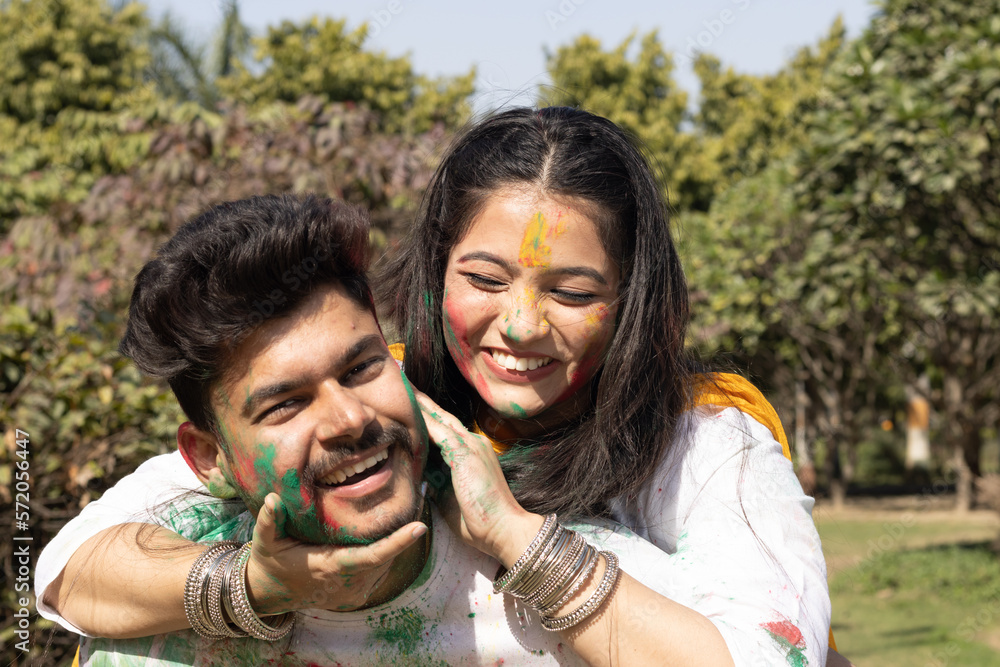 Fototapeta premium A young couple friends family boy girl man woman celebrating enjoying holi festival of colors colours with gulal abeer color powder outdoor in a park, a popular hindu festival celebrated across india