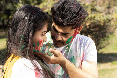 A young couple friends family boy girl man woman celebrating enjoying holi festival of colors colours with gulal abeer color powder outdoor in a park, a popular hindu festival celebrated across india