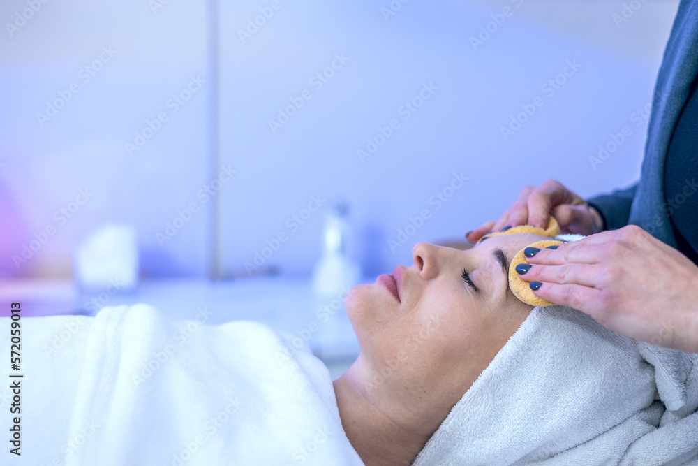 Cosmetology. The hands of a cosmetologist apply a cleansing mask for the face. Smiling girl on facial cleansing procedure Cosmetology. The hands of a cosmetologist apply a cleansing mask for the face. Smiling girl on facial cleansing procedure