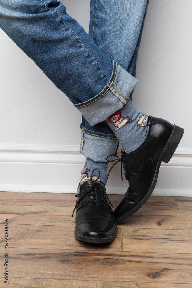 Product photos of men's footwear. Close up photo of a man's foot and legs. He is wearing blue jeans, colorful blue socks and black dress shoes. His legs are crossed. Product photos of men's footwear. Close up photo of a man's foot and legs. He is wearing blue jeans, colorful blue socks and black dress shoes. His legs are crossed.